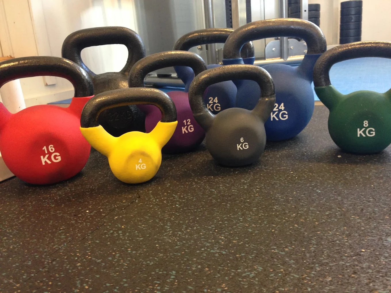 Fargerike kettlebells i ulike vektklasser står på rekke på treningsgulv
